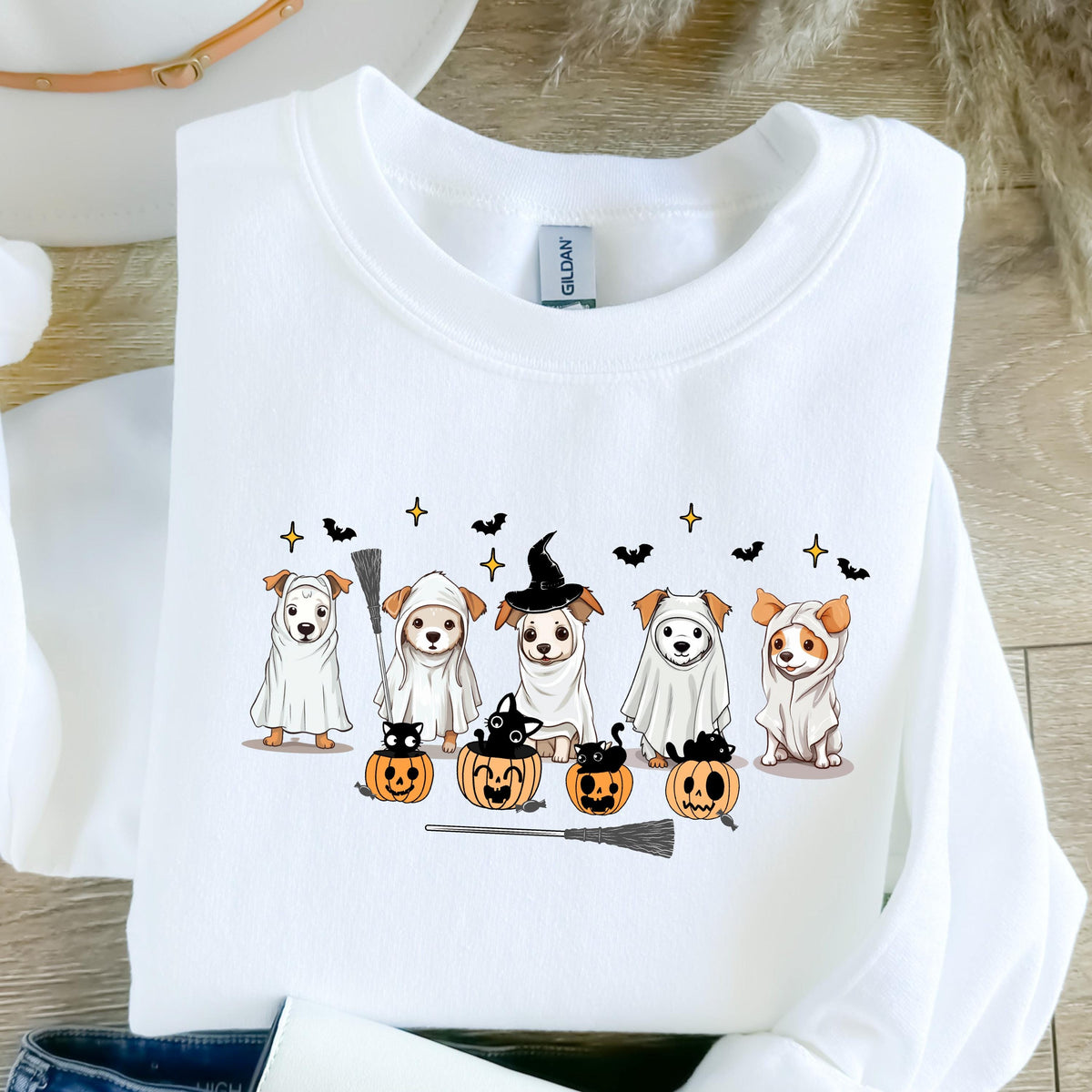 May include: White sweatshirt featuring a Halloween-themed design. The graphic includes cartoon dogs in costumes, such as ghosts and a witch, with pumpkins and bats. A broom is also included in the design.
