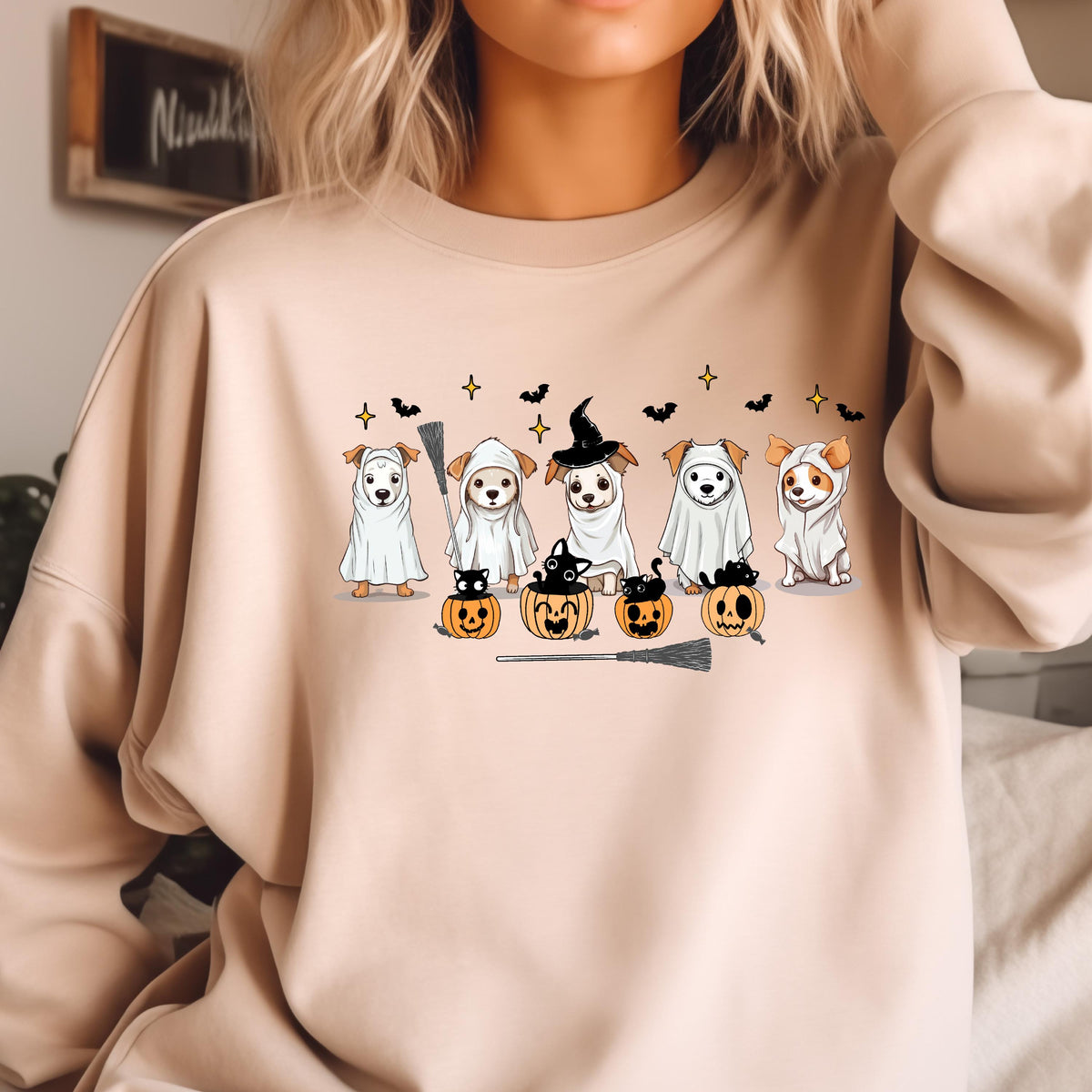 May include: Beige sweatshirt featuring a Halloween-themed graphic. The design includes six dogs dressed in costumes, including ghosts and a witch. Pumpkins, bats, and a broom complete the festive illustration.