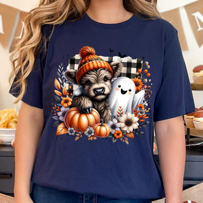 May include: A navy blue t-shirt featuring a graphic of a fluffy highland cow wearing an orange knit hat, a small white ghost, two orange pumpkins, and various autumn flowers set against a black and white buffalo plaid background.