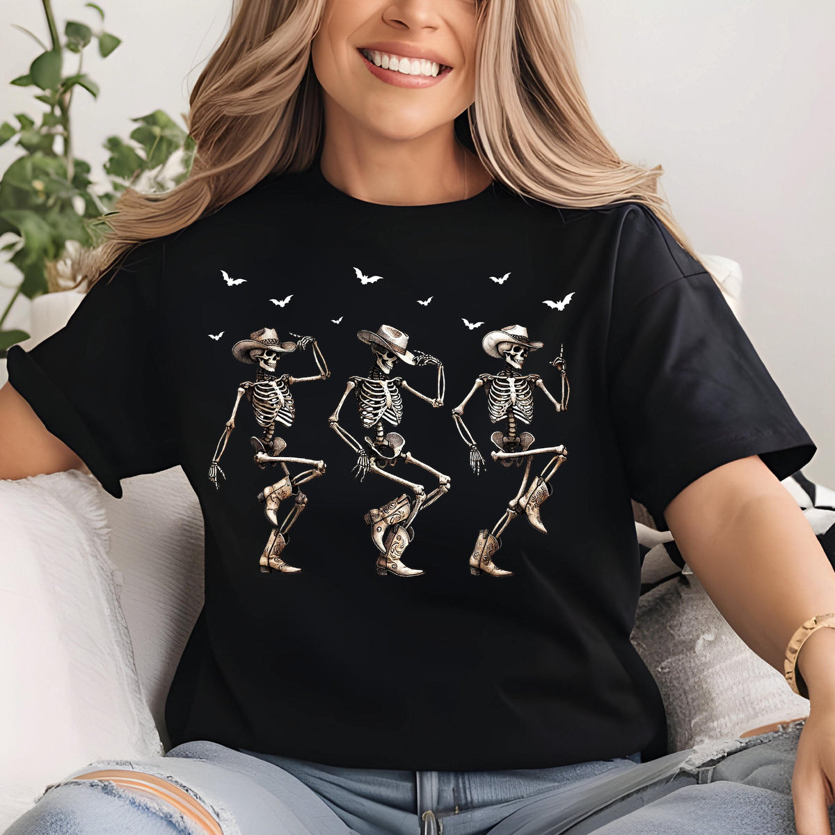 May include: Black t-shirt featuring a graphic of three dancing skeletons wearing cowboy hats and boots. White bats are flying above the skeletons. The skeletons are in various dance poses.