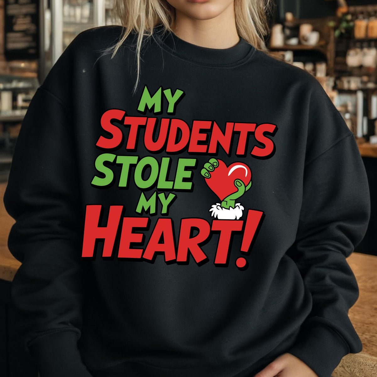 May include: Black sweatshirt with the text "MY STUDENTS STOLE MY HEART!" in red and green. The design includes a green hand holding a red heart. The sweatshirt is a crew neck style.