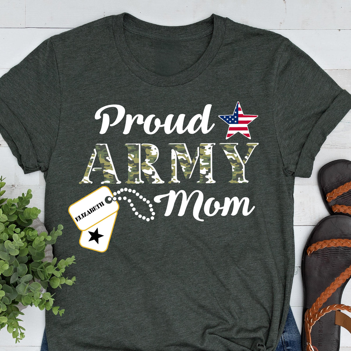 May include: Dark gray t-shirt with the words "Proud ARMY Mom" in white. The word "ARMY" is in a camouflage pattern. A star with the American flag design is above the word "ARMY". A dog tag with the name "Elizabeth" is also featured.