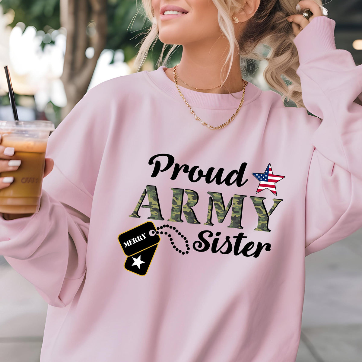 May include: A light pink sweatshirt with the words "Proud ARMY Sister" in black and camouflage green. An American flag star graphic and a dog tag graphic are also featured on the front.