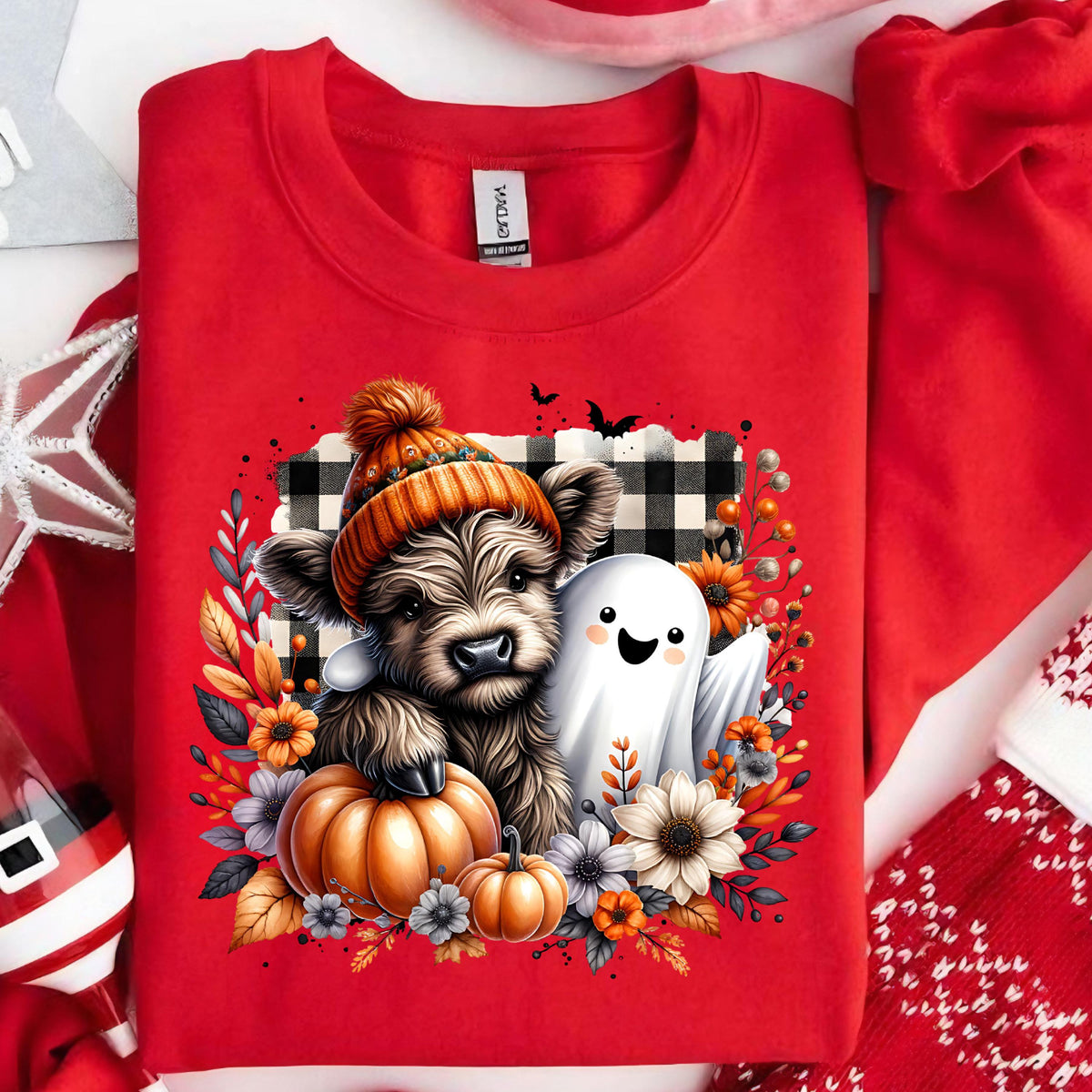 May include: A bright red crewneck sweatshirt featuring a graphic of a fluffy Highland cow wearing an orange knit hat, sitting next to a white ghost. The design includes a large orange pumpkin, autumn flowers, and a black and white buffalo plaid square.