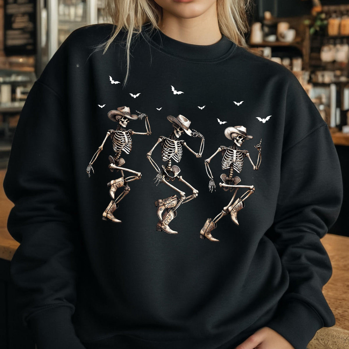May include: Black sweatshirt featuring a graphic of three dancing skeletons wearing cowboy hats and boots. White bats are scattered across the top. The skeletons are in various dance poses, with detailed bone structures.