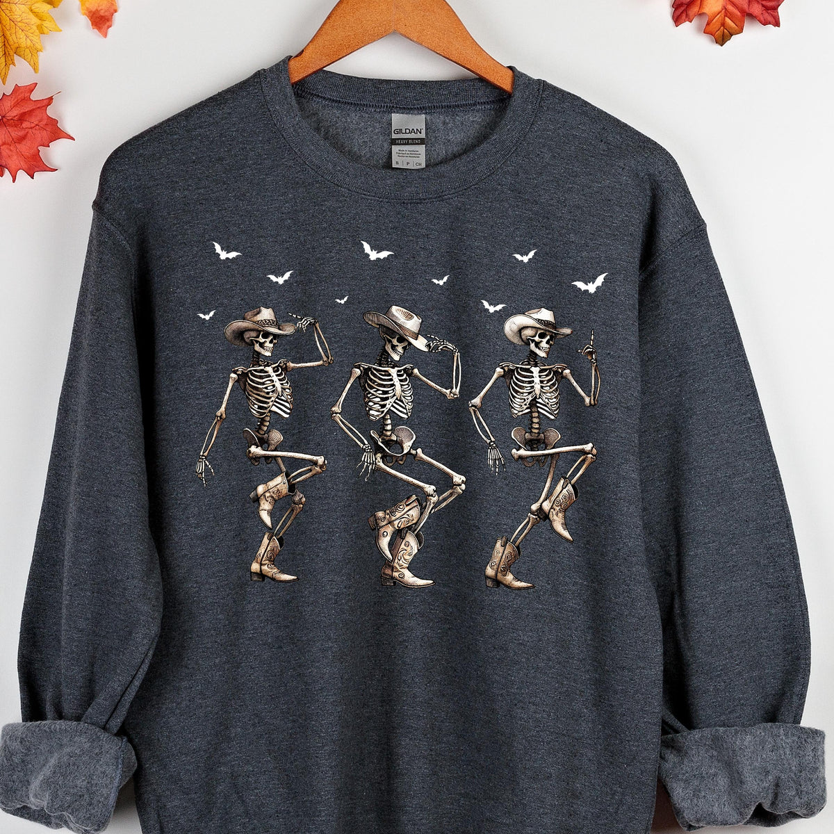 May include: Dark gray sweatshirt featuring a graphic of three dancing skeletons wearing cowboy hats and boots. White birds are scattered across the top. The sweatshirt has a crew neck and long sleeves.