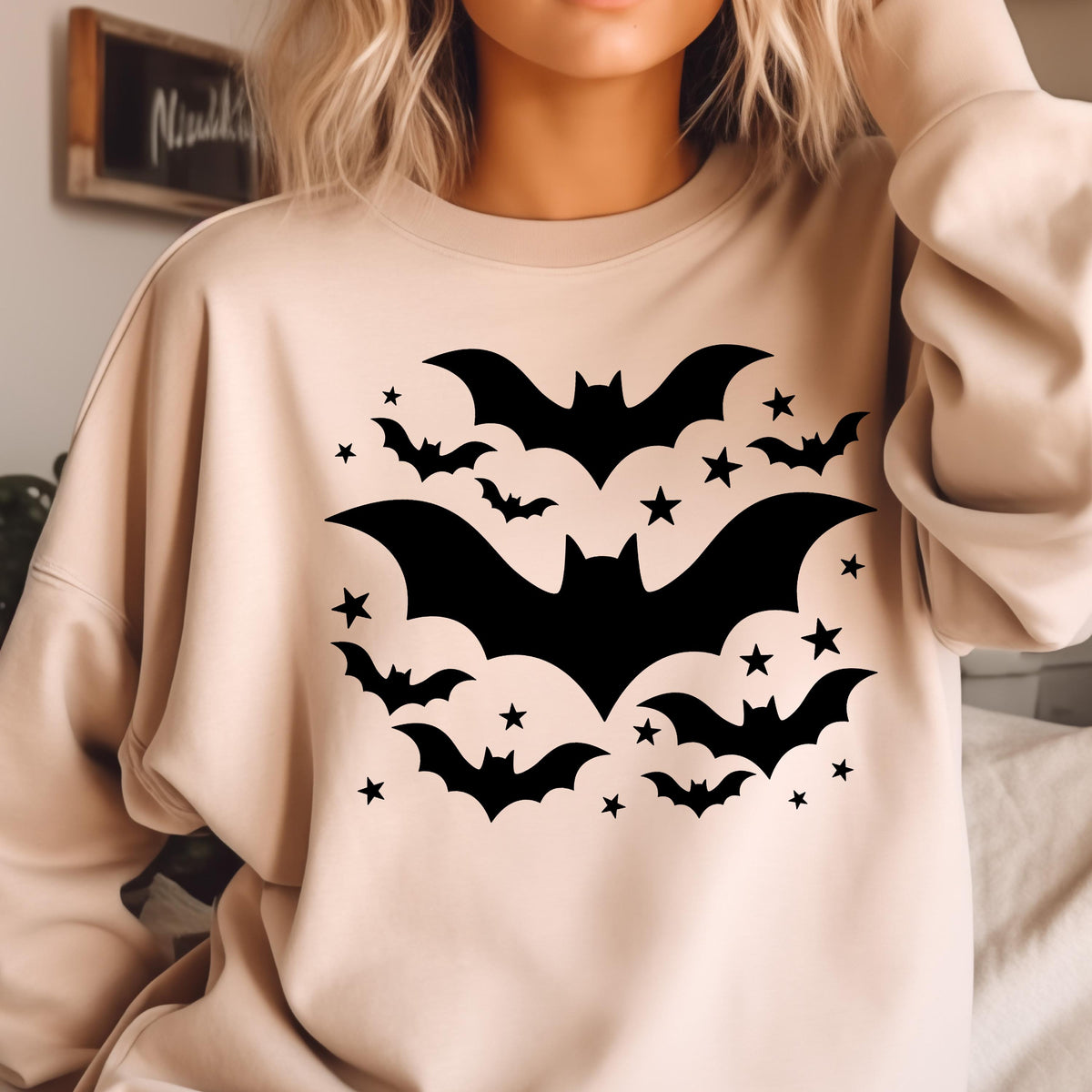 May include: Beige sweatshirt featuring a black bat and star design. The graphic includes several bats of varying sizes and numerous stars. The design is centered on the front of the sweatshirt, creating a Halloween theme.