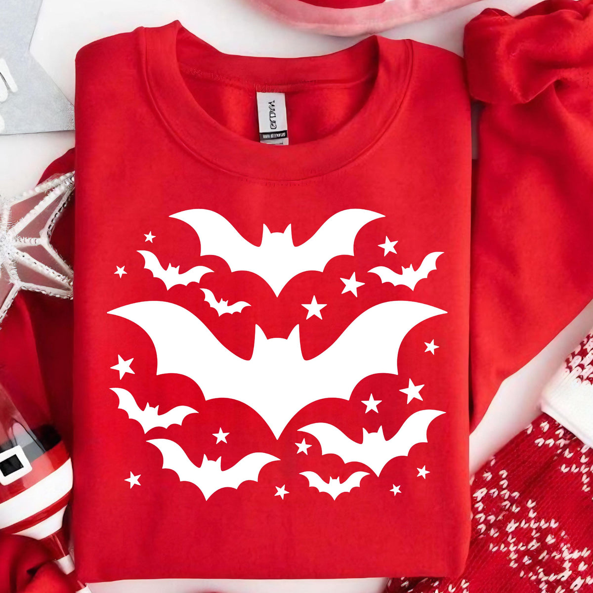 May include: A red sweatshirt featuring a white bat and star design. The graphic includes several bats of varying sizes and small stars, creating a Halloween or spooky theme. The sweatshirt is a crew neck style.