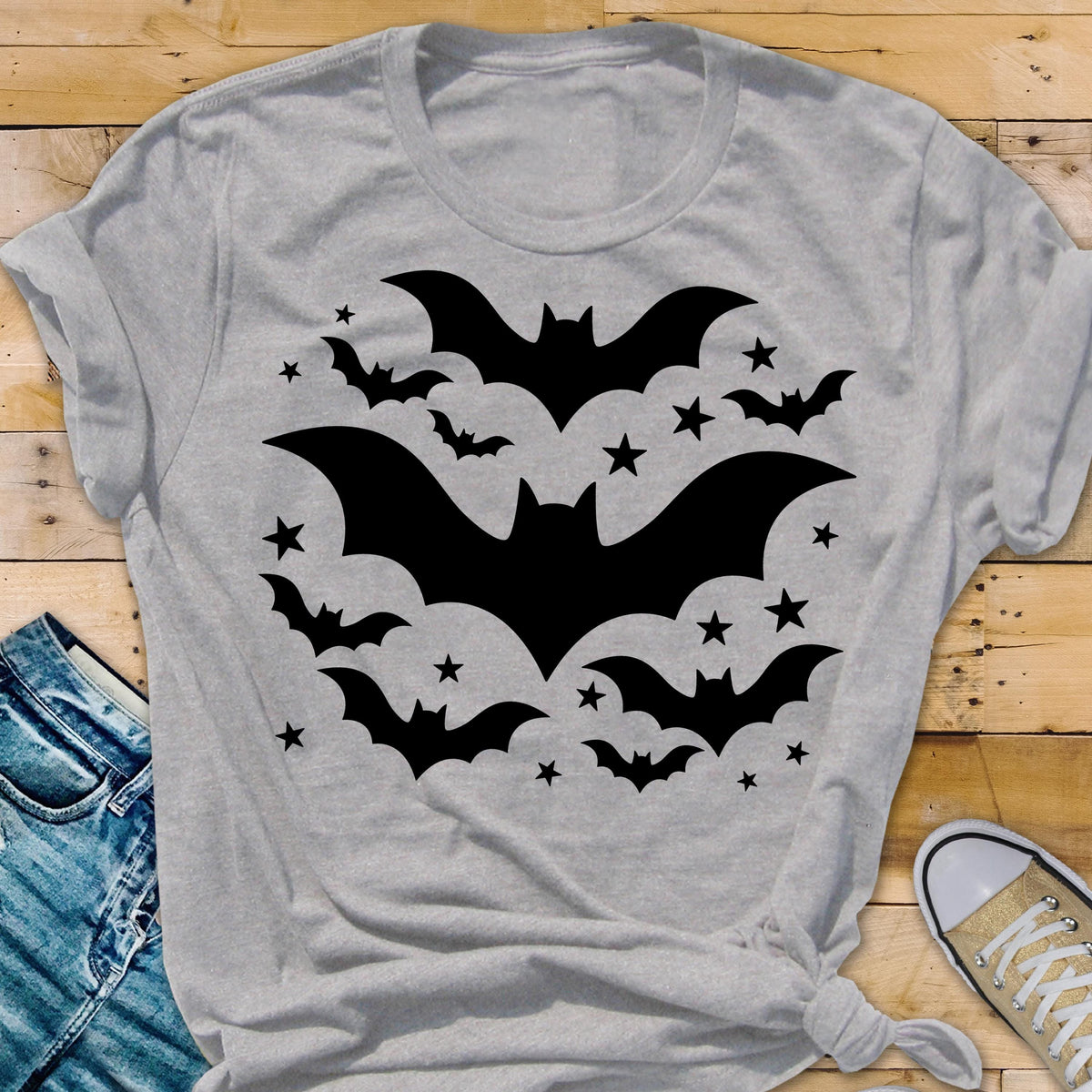 May include: A light gray t-shirt featuring a black bat and star design. The graphic includes several bats of varying sizes and stars, creating a Halloween-themed design. The shirt is made of a soft material.