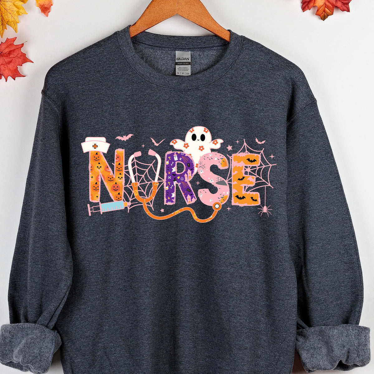 May include: Dark gray sweatshirt with a Halloween-themed design. The word "Nurse" is spelled out in colorful letters, with a stethoscope, ghost, bats, and spiderwebs. The design is printed on the front of the sweatshirt.