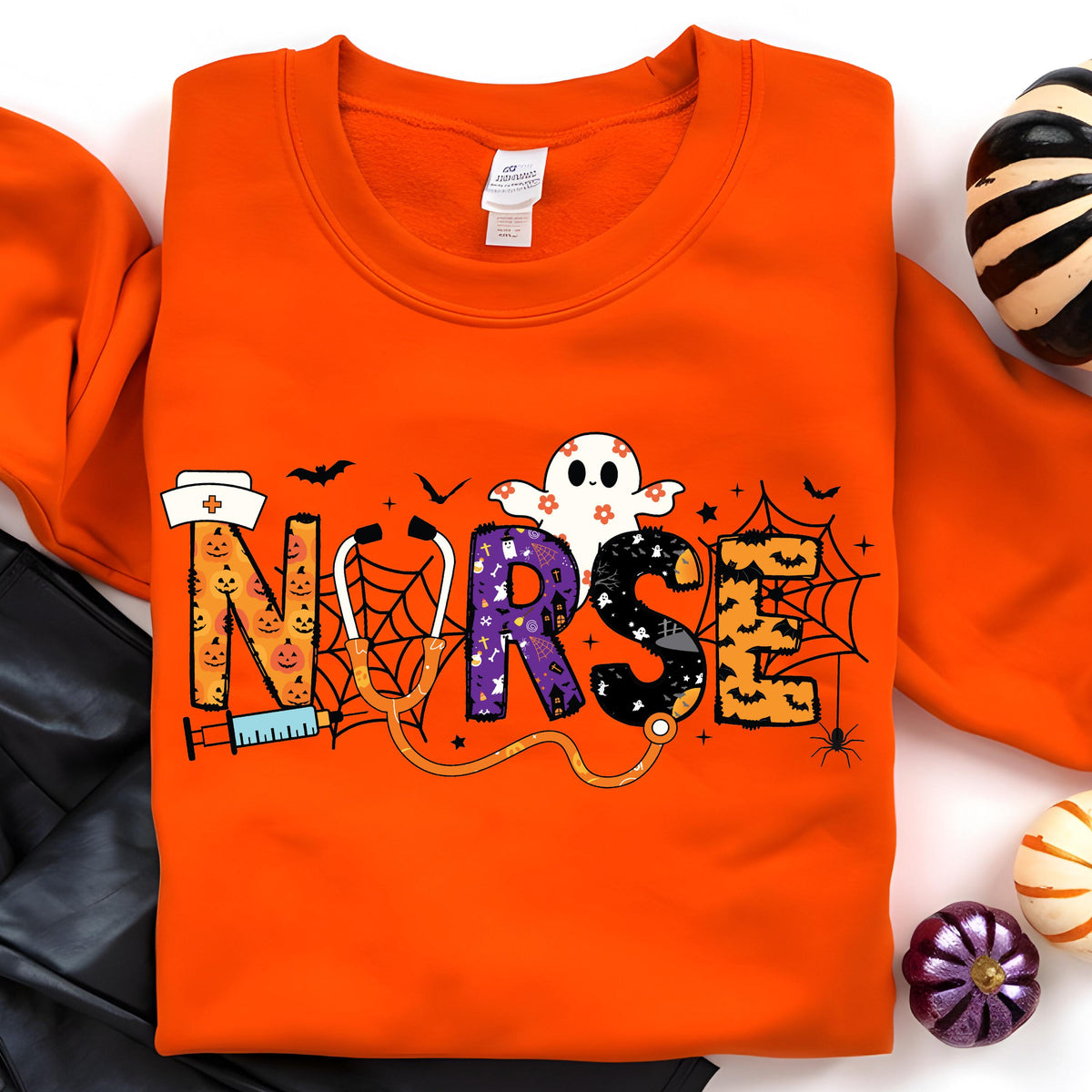 May include: An orange sweatshirt with the word "NURSE" in a Halloween-themed design. The letters are decorated with pumpkins, a ghost, bats, and spiderwebs. A stethoscope and syringe are also included in the design.