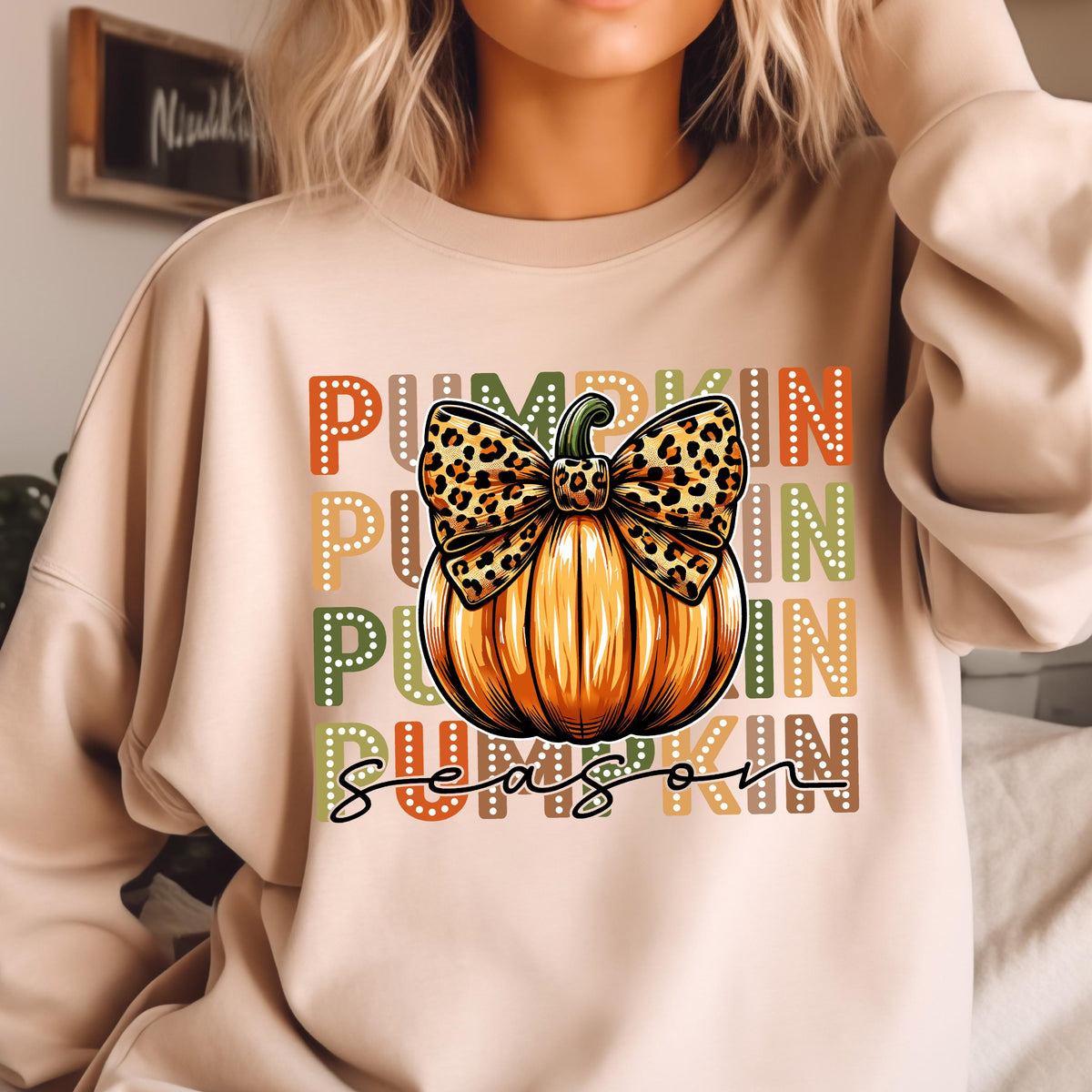 May include: Beige sweatshirt with a pumpkin graphic. The pumpkin is orange with a leopard print bow. The words "PUMPKIN SEASON" are printed in orange, yellow, green, and brown. The sweatshirt is a fall-themed design.
