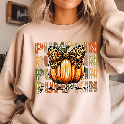 May include: Beige sweatshirt with a pumpkin graphic. The pumpkin is orange with a leopard print bow. The words "PUMPKIN SEASON" are printed in orange, yellow, green, and brown. The sweatshirt is a fall-themed design.