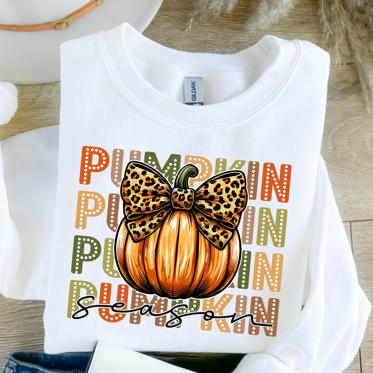 May include: White sweatshirt featuring a pumpkin graphic with a leopard print bow. The word "PUMPKIN" is stacked vertically in orange, green, and brown. The word "Season" is written in a script font below the pumpkin.
