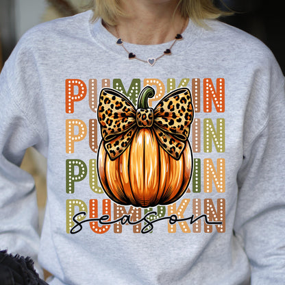 May include: A light gray sweatshirt featuring a large orange pumpkin with a leopard print bow. The word "PUMPKIN" is printed vertically in orange and green, and "season" is written in black script.