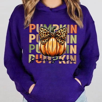 May include: A purple hooded sweatshirt featuring a graphic of a pumpkin with a leopard print bow. The words "PUMPKIN SEASON" are printed in a stacked design with orange, green, and white dotted letters.