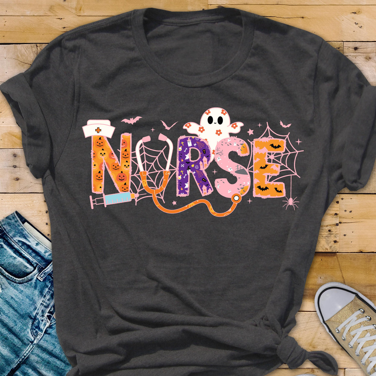 May include: Dark gray t-shirt with a Halloween-themed "NURSE" design. The word "NURSE" is spelled out with orange, purple, and pink letters, featuring a ghost, bats, spiderwebs, and a stethoscope.