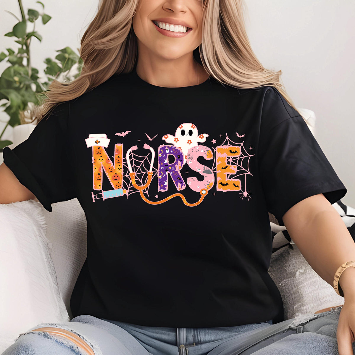 May include: Black t-shirt with the word "NURSE" in colorful, Halloween-themed lettering. The design includes a ghost, spiderwebs, bats, and a stethoscope. The letters are orange, purple, and pink.
