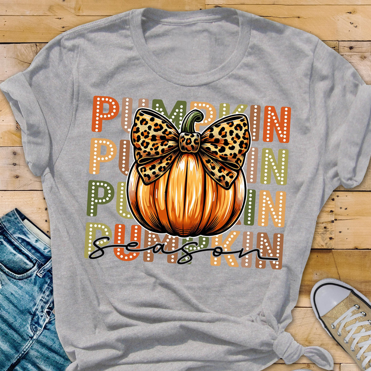 May include: A gray t-shirt featuring a large orange pumpkin with a leopard print bow. The words "PUMPKIN SEASON" are printed in orange, green, and white. The shirt is a casual style.
