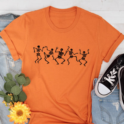 May include: An orange t-shirt featuring a black graphic of dancing skeletons. The skeletons are in various poses, with arms and legs outstretched. The shirt is made of a soft material and has a classic crew neck design.