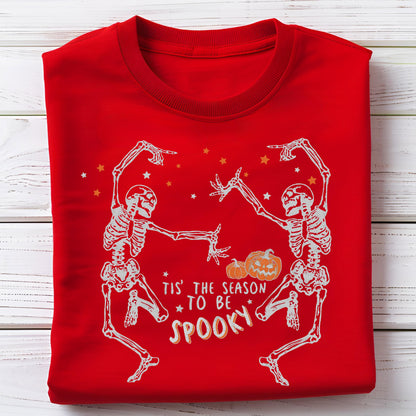 May include: Red sweatshirt with a white skeleton design. Two skeletons are dancing, with pumpkins and stars. The text reads "Tis' the season to be spooky."