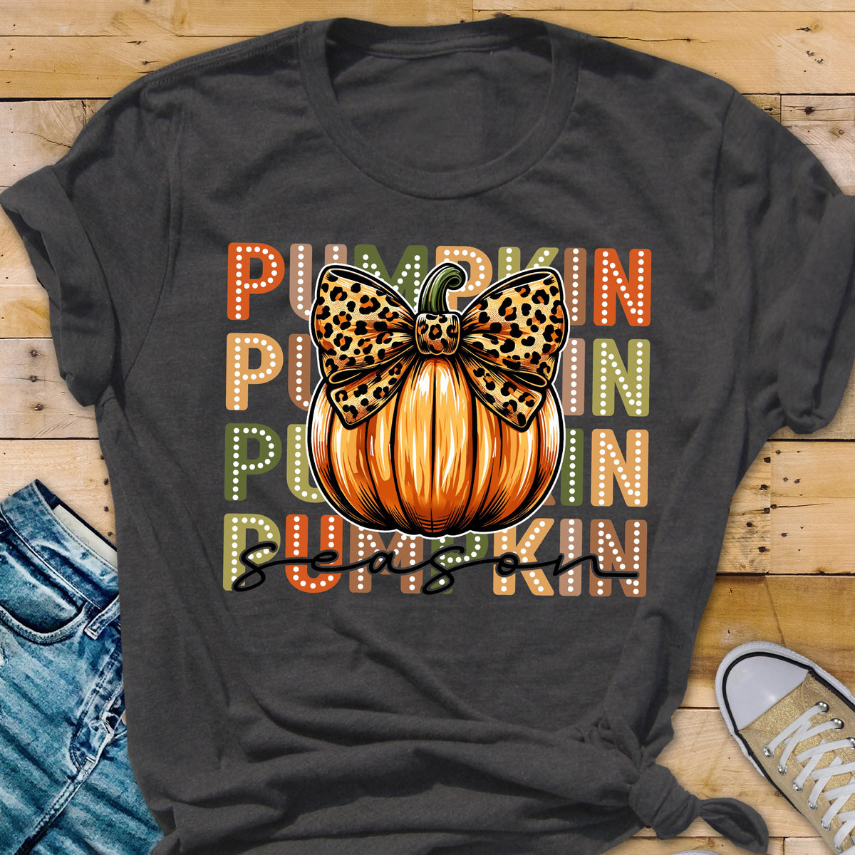 May include: Dark gray t-shirt featuring a large orange pumpkin with a leopard print bow. The word "PUMPKIN" is stacked vertically in orange, green, and brown. The words "PUMPKIN SEASON" are written in a script font.