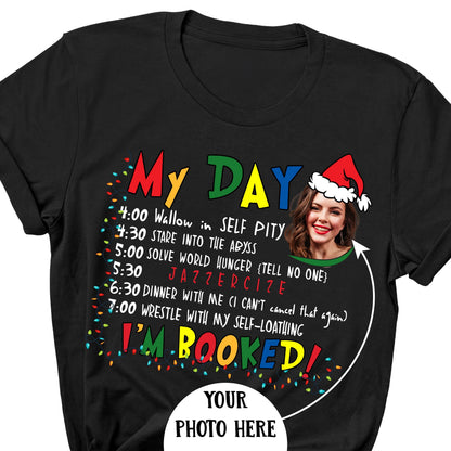 May include: Black t-shirt with the text "My Day" in colorful letters. The shirt features a humorous schedule including "Wallow in Self Pity" and "Jazzericize." A photo of a woman wearing a Santa hat is also included.
