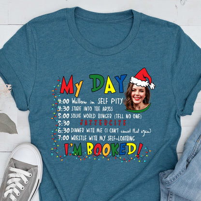 May include: Teal t-shirt with the text "My Day" and a schedule of humorous activities. The schedule includes "Wallow in SELF PITY," "Stare into the Abyss," and "JAZZERCIZE." A woman wearing a Santa hat is in the image.