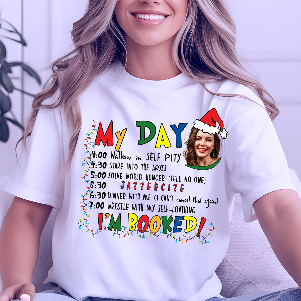 May include: White t-shirt with the text "My Day" in colorful letters and a schedule of humorous activities. The schedule includes "Wallow in Self Pity" and "Jazzerize". A woman wearing a Santa hat is in the image.
