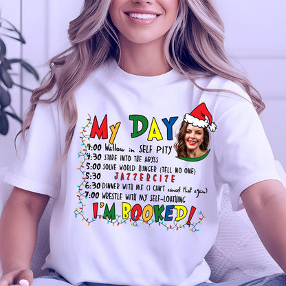 May include: White t-shirt with the text "My Day" in colorful letters and a schedule of humorous activities. The schedule includes "Wallow in Self Pity" and "Jazzerize". A woman wearing a Santa hat is in the image.