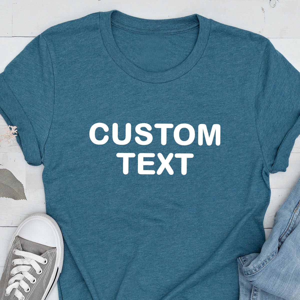 May include: A heathered teal short-sleeve t-shirt featuring the words CUSTOM TEXT printed in bold white capital letters across the center of the chest. The shirt has a crew neckline and a standard fit, showcasing a simple and clean design.