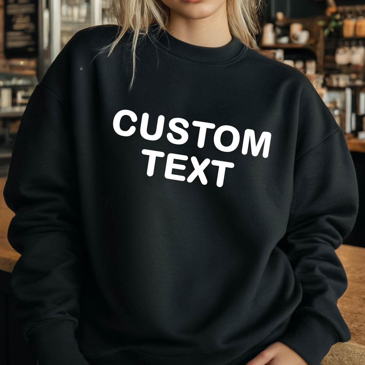 May include: A black long-sleeve crewneck sweatshirt featuring the words CUSTOM TEXT printed in bold white capital letters across the chest. The garment has a ribbed neckline, cuffs, and hem, providing a standard fit with long sleeves.