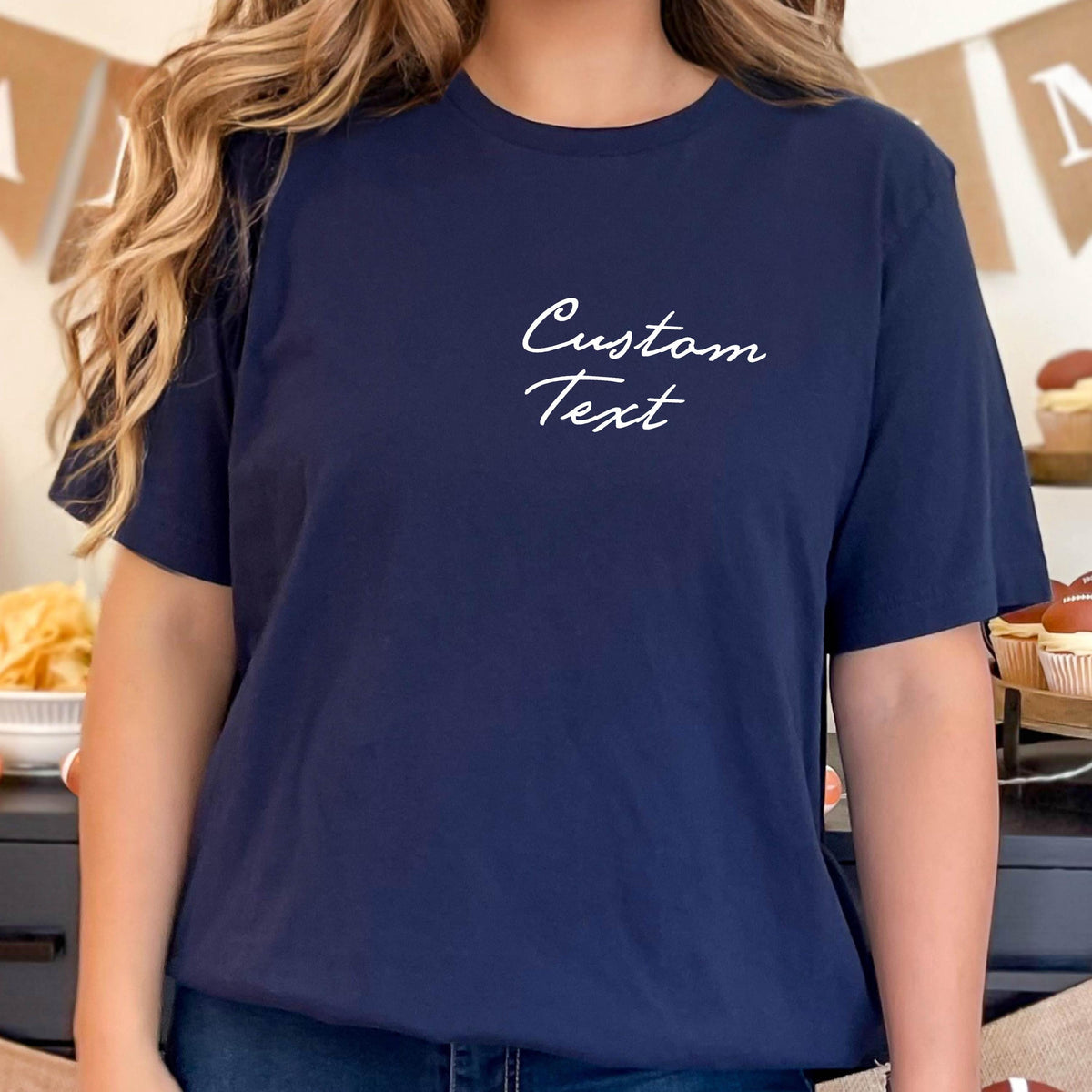 May include: Navy blue t-shirt with the words "Custom Text" in white script. The shirt is a solid color and has a classic crew neck design. The image shows a close-up of the shirt, highlighting the text and fabric.