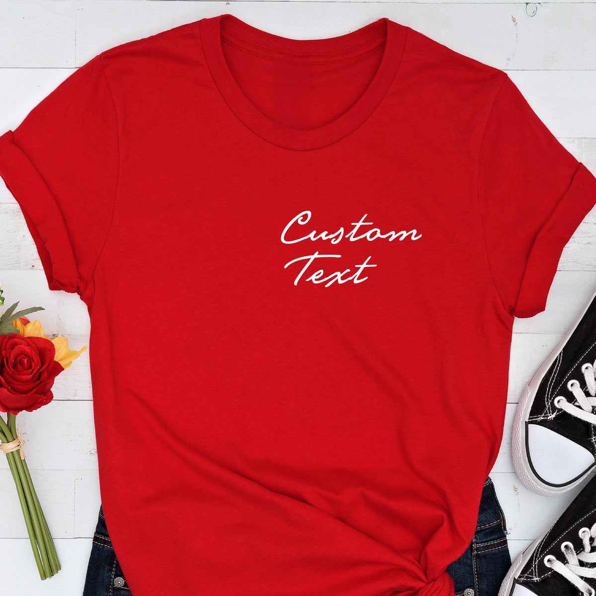 May include: A bright red t-shirt with the words "Custom Text" in white script. The shirt has short sleeves and a crew neck. A pair of black canvas sneakers with white soles are visible in the bottom right corner.