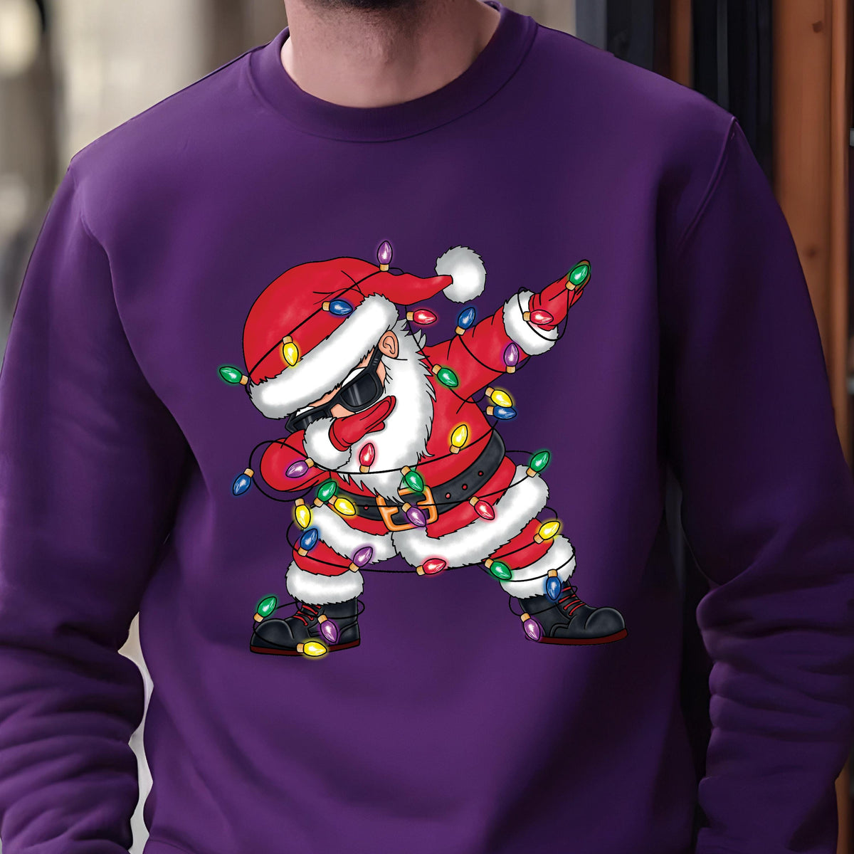 May include: Purple sweatshirt with a cartoon image of Santa Claus wearing sunglasses and tangled in Christmas lights. Santa is in a dabbing pose.