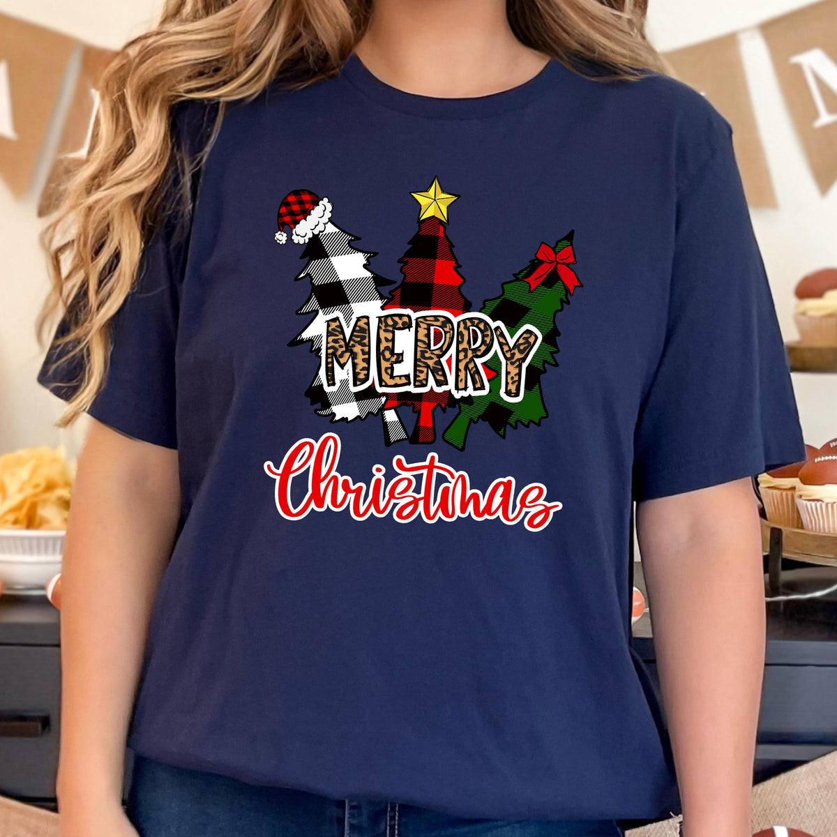 May include: A navy blue t-shirt featuring a graphic of three stylized Christmas trees in black and white buffalo plaid, red and black buffalo plaid, and green patterns. The text MERRY is in leopard print, and Christmas is in red script.