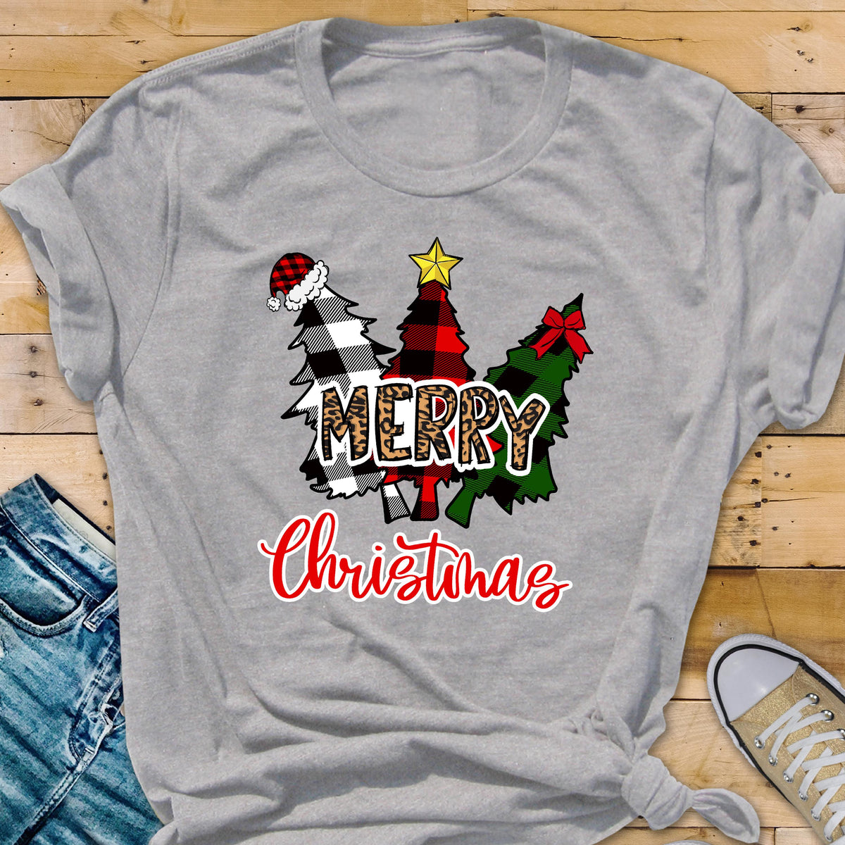 May include: A light gray t-shirt featuring a graphic of three stylized Christmas trees in black and white buffalo plaid, red and black plaid, and green plaid. The word MERRY is in leopard print, and the word Christmas is in red script.