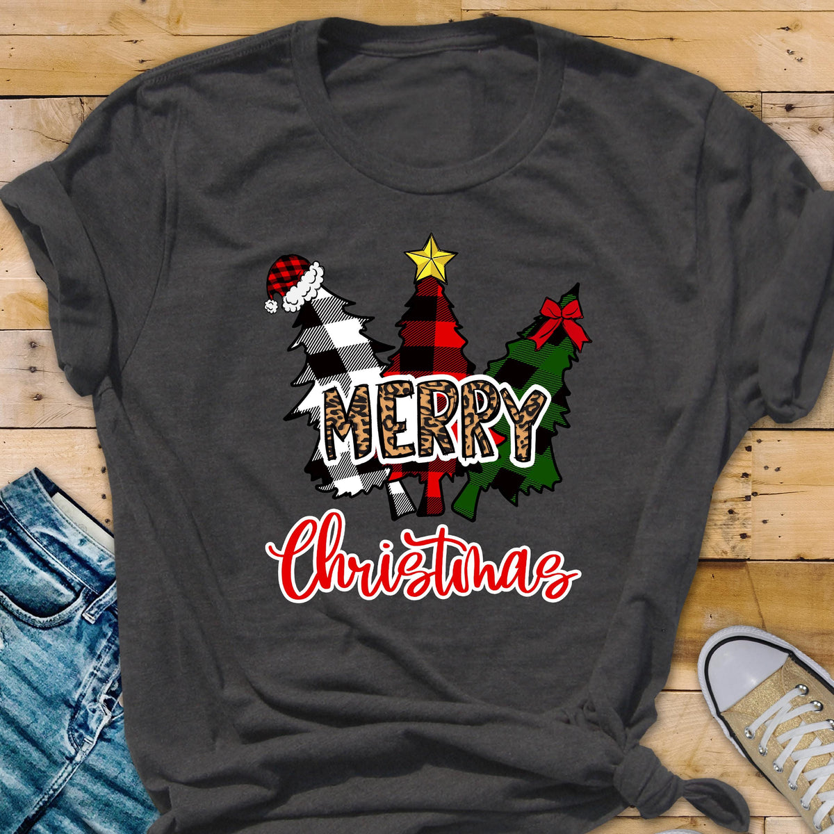 May include: A dark gray t-shirt featuring a graphic of three stylized Christmas trees. The trees are decorated with a red and black buffalo plaid pattern, a black and white buffalo plaid pattern, and a solid green color with a red bow and a yellow star.