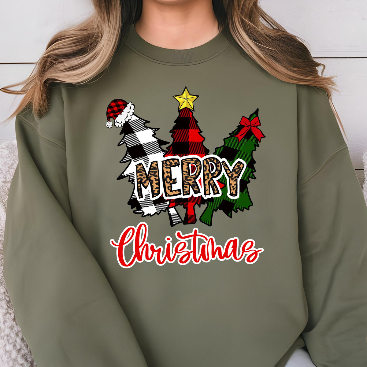 May include: An olive green crewneck sweatshirt featuring a graphic of three stylized Christmas trees in black and white, red and black, and green and black buffalo plaid patterns. The word MERRY is in leopard print, and Christmas is in red.