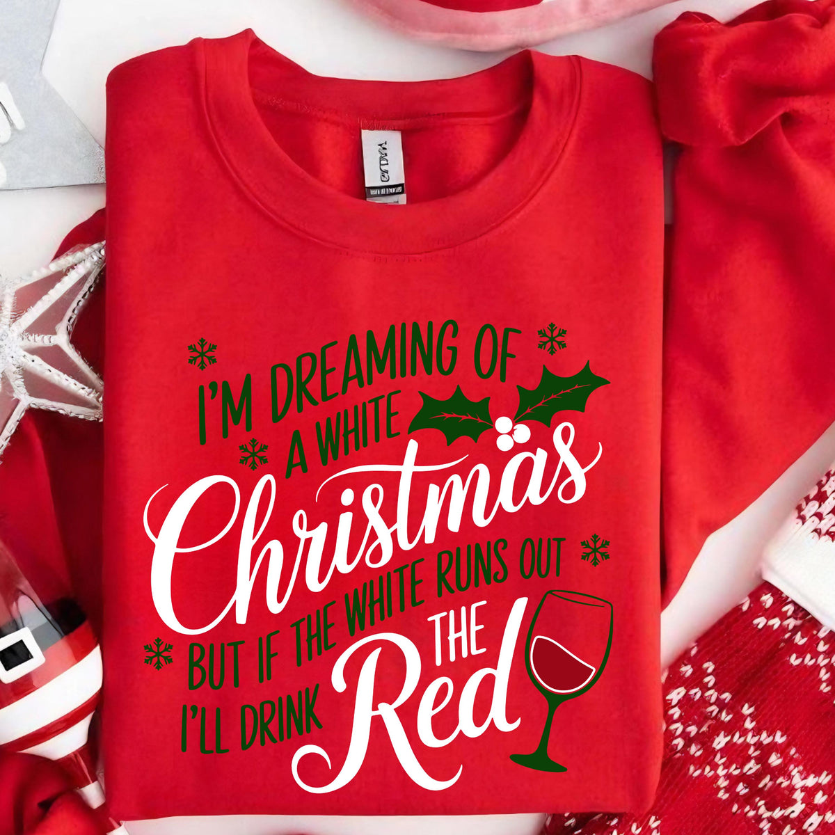 May include: A red crewneck sweatshirt featuring green and white text that reads I'M DREAMING OF A WHITE Christmas BUT IF THE WHITE RUNS OUT I'LL DRINK THE Red. The design includes green holly leaves, small snowflakes, and a graphic of a wine glass.
