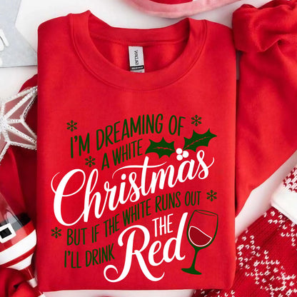 May include: A red crewneck sweatshirt featuring green and white text that reads I'M DREAMING OF A WHITE Christmas BUT IF THE WHITE RUNS OUT I'LL DRINK THE Red. The design includes green holly leaves, small snowflakes, and a graphic of a wine glass.