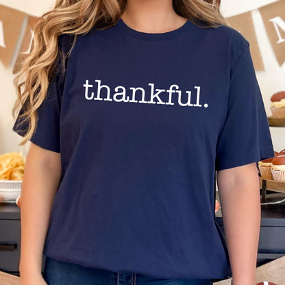 May include: Navy blue t-shirt with the word "thankful" printed in white. The shirt has short sleeves and a crew neck. The text is centered on the front of the shirt.