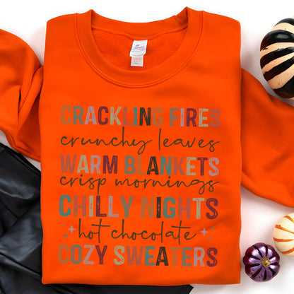 May include: Orange sweatshirt with a colorful graphic print that reads "Crackling Fires, Crunchy Leaves, Warm Blankets, Crisp Mornings, Chilly Nights, Hot Chocolate, Cozy Sweaters".