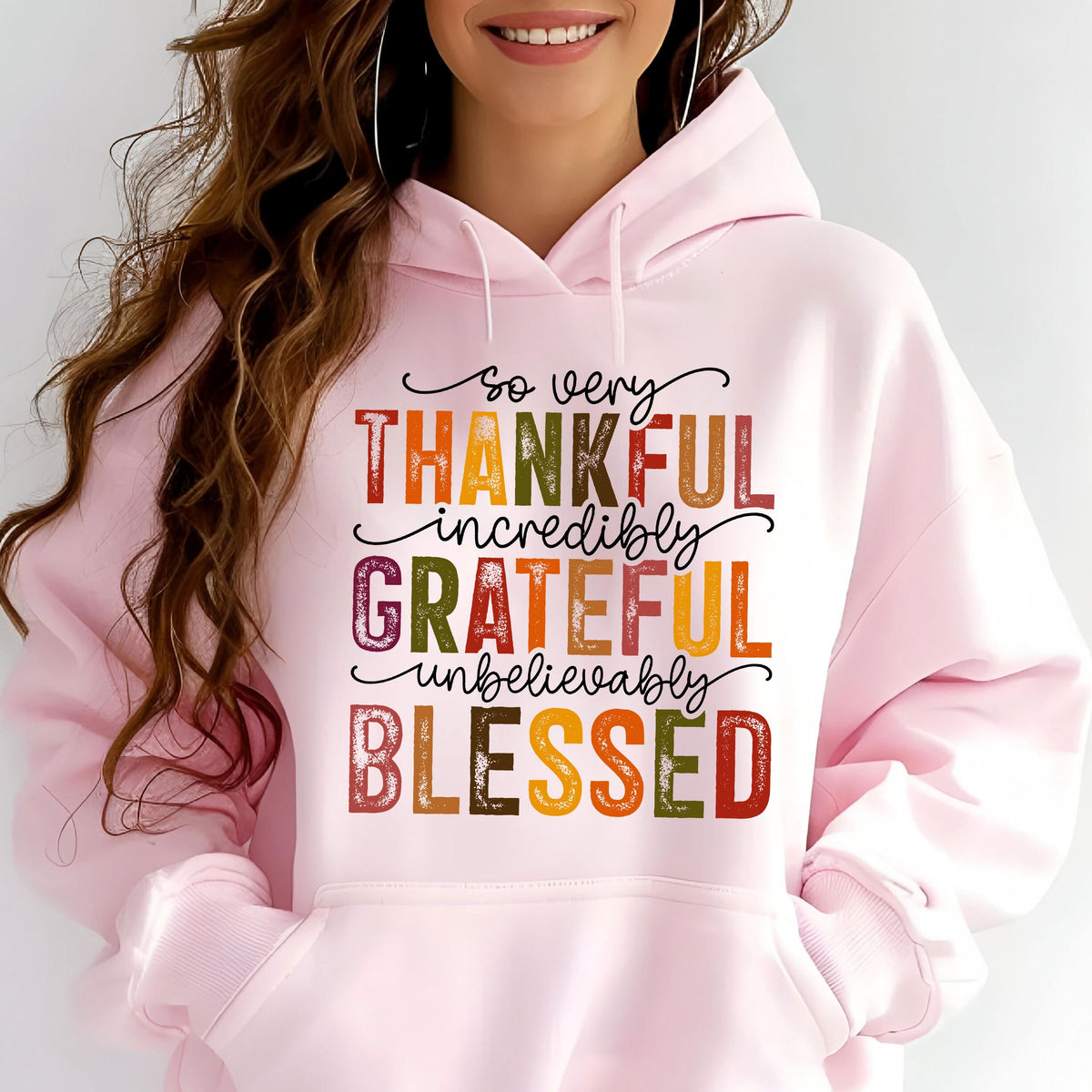 May include: A light pink hooded sweatshirt featuring a front graphic with the text so very THANKFUL incredibly GRATEFUL unbelievably BLESSED in a multi-colored, distressed font. The hoodie includes a drawstring hood and a large front kangaroo pocket.