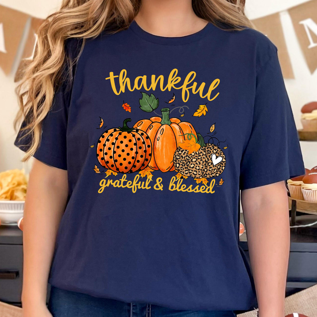 May include: Navy blue t-shirt featuring a fall-themed graphic. The design includes three pumpkins in orange and brown, with the words "thankful, grateful & blessed" in yellow script. The pumpkins have polka dots and leopard print.