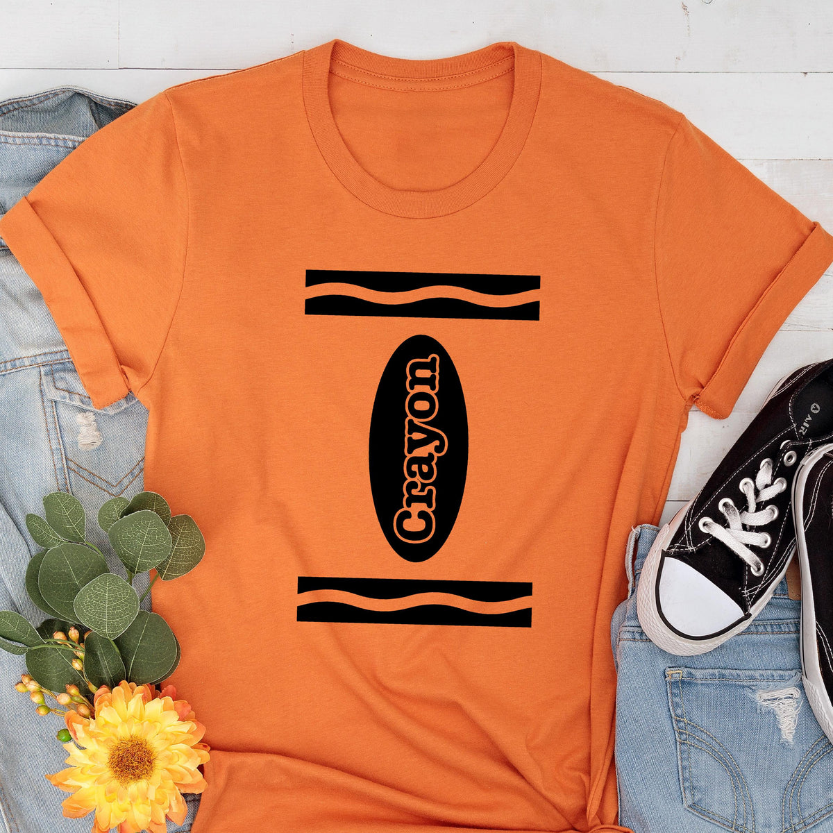 May include: Orange t-shirt with a black and white crayon design. The crayon is labeled "Crayon".