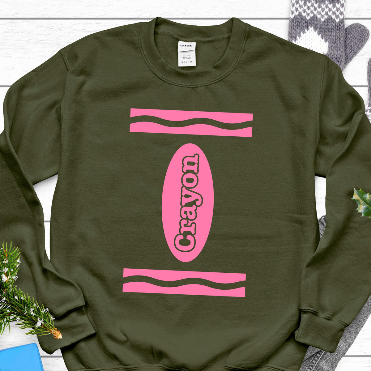 May include: A green sweatshirt with a pink crayon design. The crayon is labeled "Crayon" in pink letters.