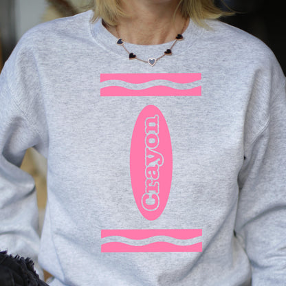 May include: A gray sweatshirt with a pink crayon design. The crayon is labeled "Crayon" and has a wavy line at the top and bottom.