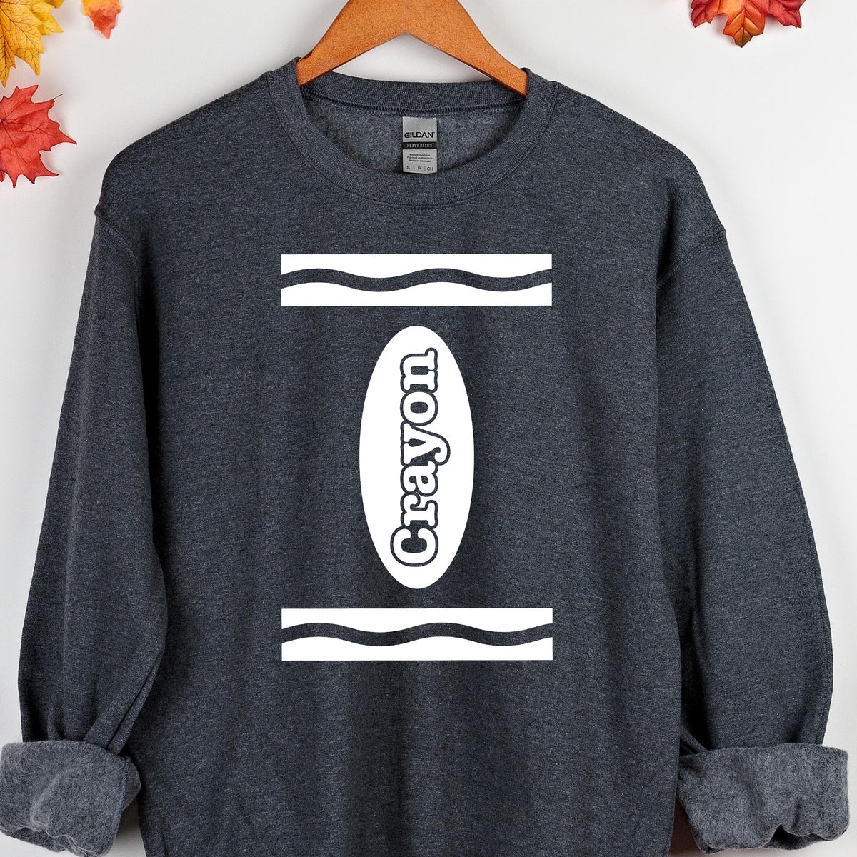 May include: A dark gray sweatshirt with a white crayon design. The design features a white oval with the word "Crayon" inside and two wavy lines above and below the oval.