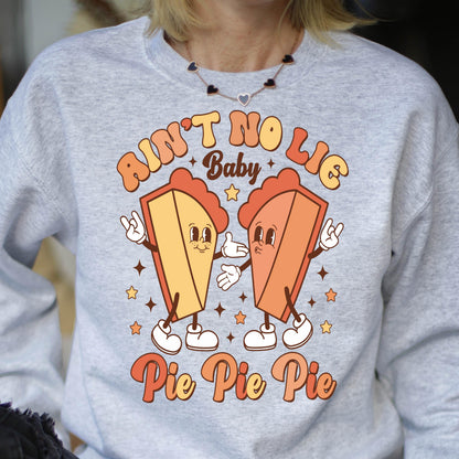 May include: A light gray crewneck sweatshirt featuring a graphic print of two anthropomorphic pie slices with arms and legs. The text reads AIN'T NO LIE Baby Pie Pie Pie. The pie slices are yellow and orange with white gloves and shoes.